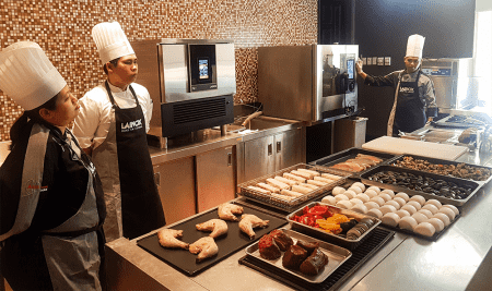 three cooks in a kitchen with raw foods on the table