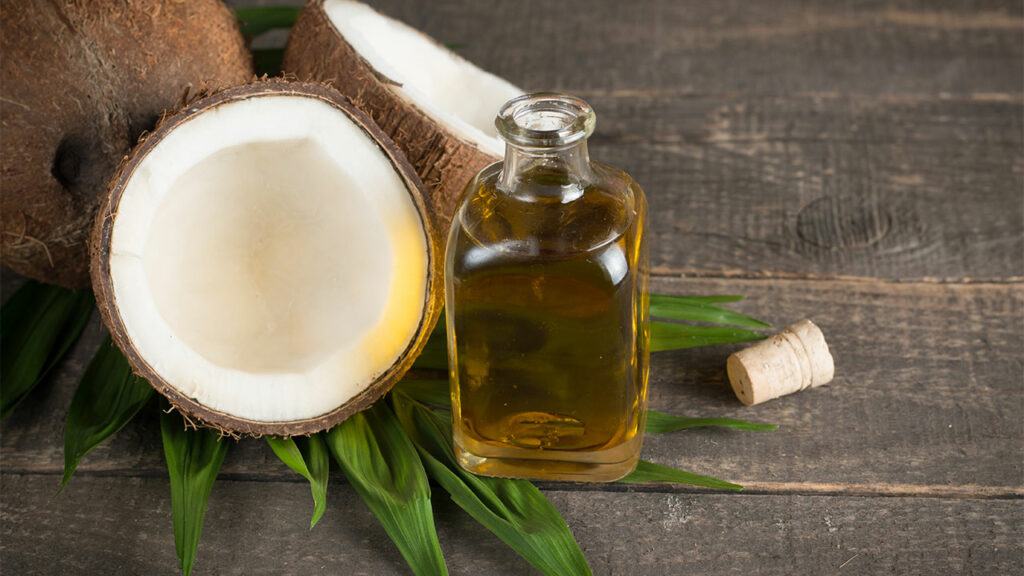 coconut oil in glass bottle with cut coconut and leaves