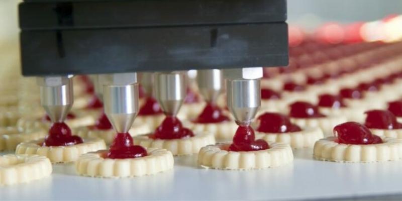 red jelly fillings being poured on biscuits by an industrial machine