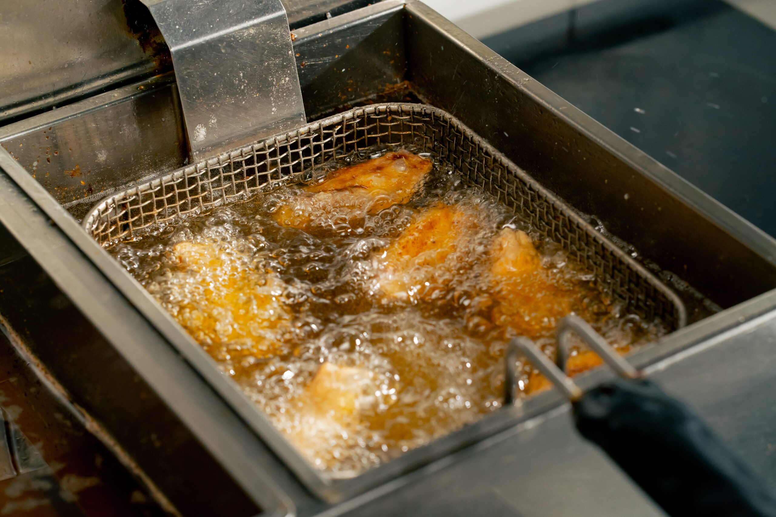 close-up in a professional kitchen frying chicken wings in oil in a deep fryer